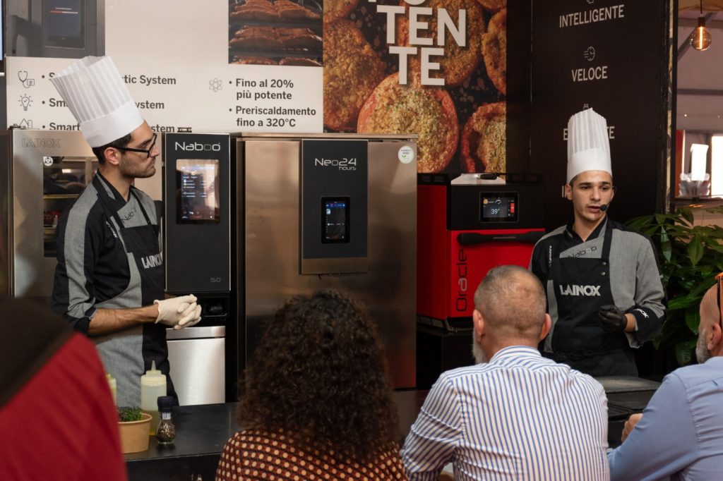 Due pizzaioli in divisa durante una dimostrazione allo stand, davanti al pubblico
