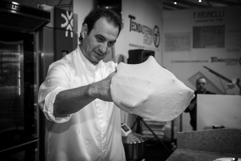 Un pizzaiolo stende un panetto di impasto allo stand