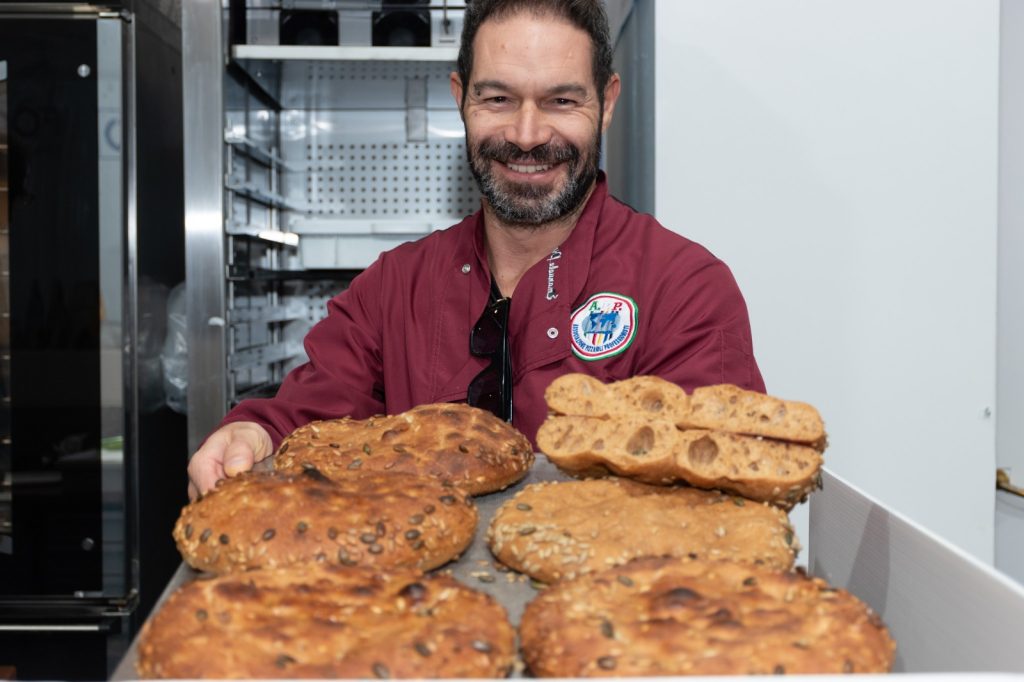 Un panettiere mostra un vassoio di focacce appena sfornate