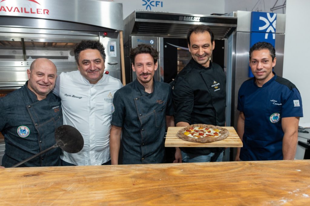 Cinque professionisti in divisa mostrano una pizza appena sfornata