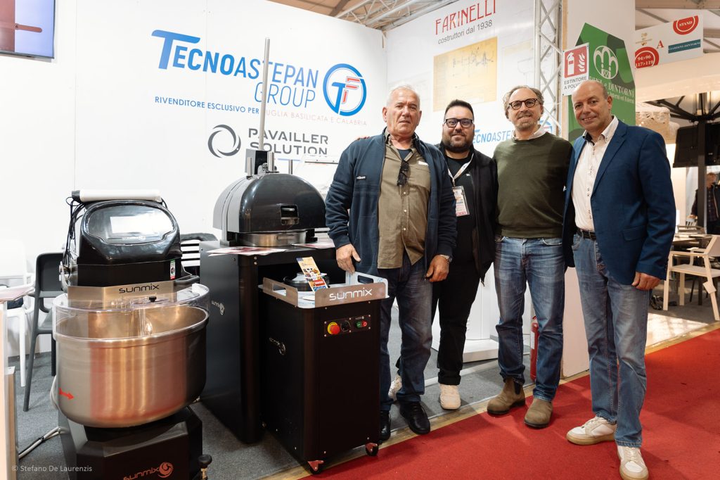Tre persone in posa davanti a un'impastatrice Sunmix allo stand