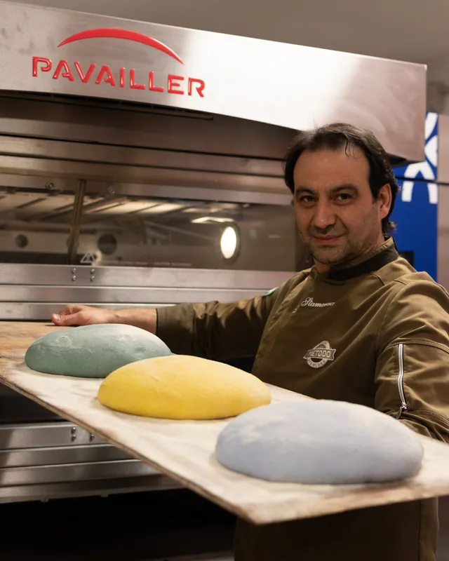 Panettiere con la pala davanti a un forno Pavailler: tre pani colorati di verde, giallo e azzurro